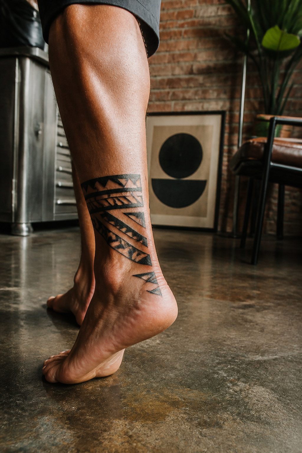 A bold tribal ankle tattoo on a male model.