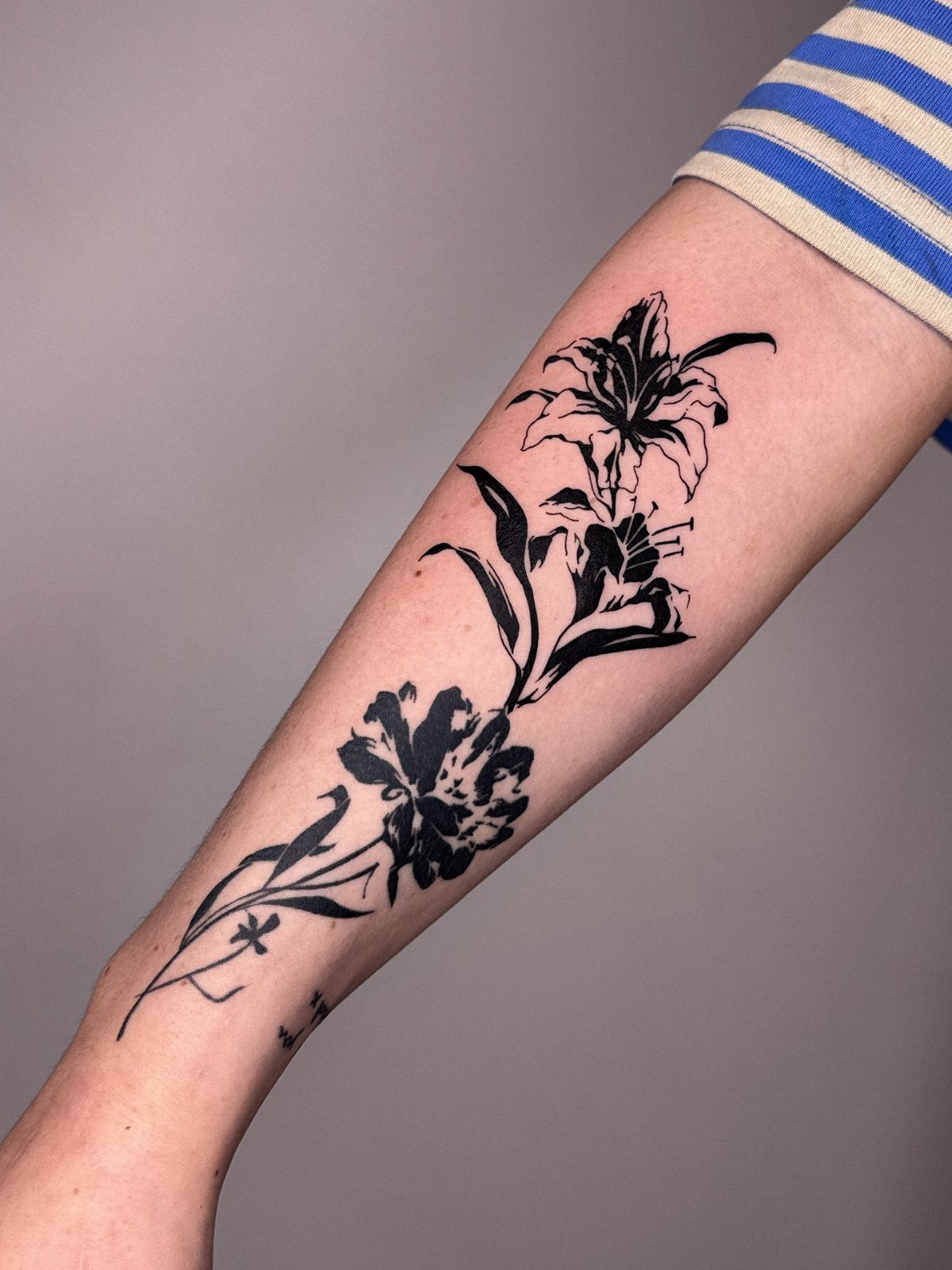 17 Flower Tattoo Ideas That Work in Every Style 10 Black ink floral tattoo featuring two large flowers and leaves on a person's forearm.