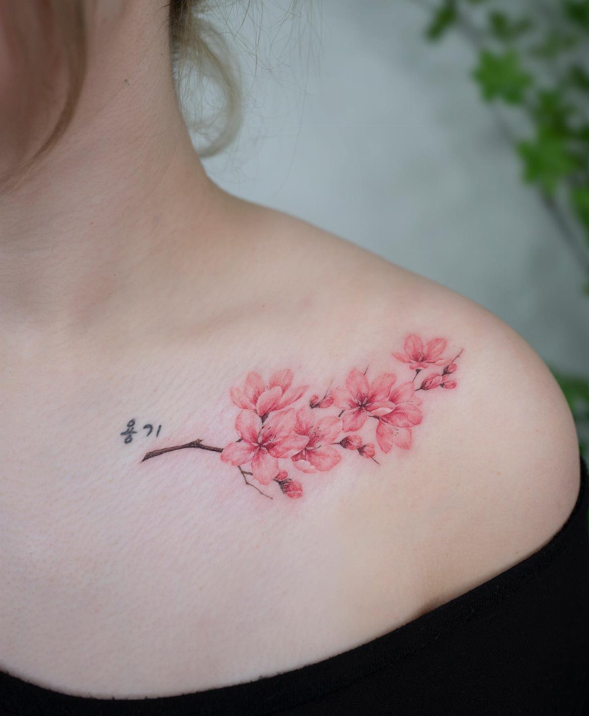 17 Flower Tattoo Ideas That Work in Every Style 2 Pink cherry blossom branch tattoo with small black text on a person's shoulder.