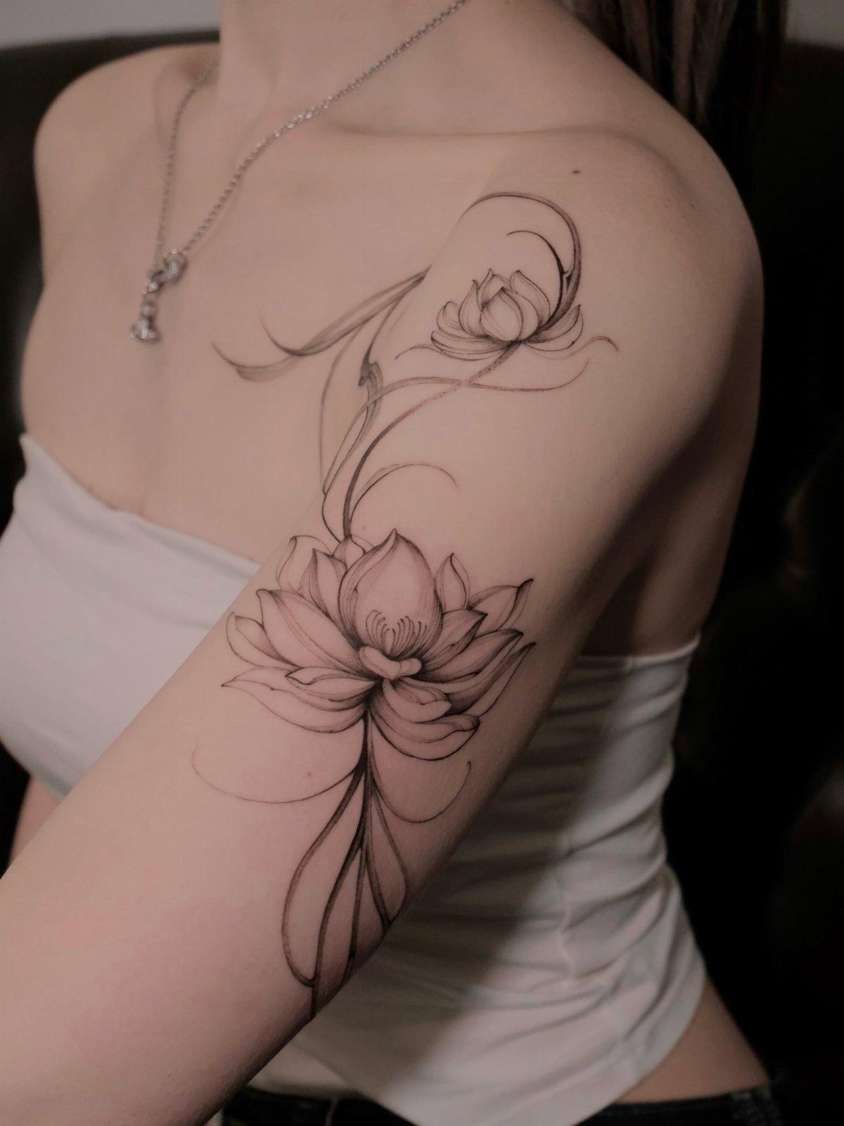 17 Flower Tattoo Ideas That Work in Every Style 12 Fine line lotus flower tattoo on a person's shoulder and upper arm.