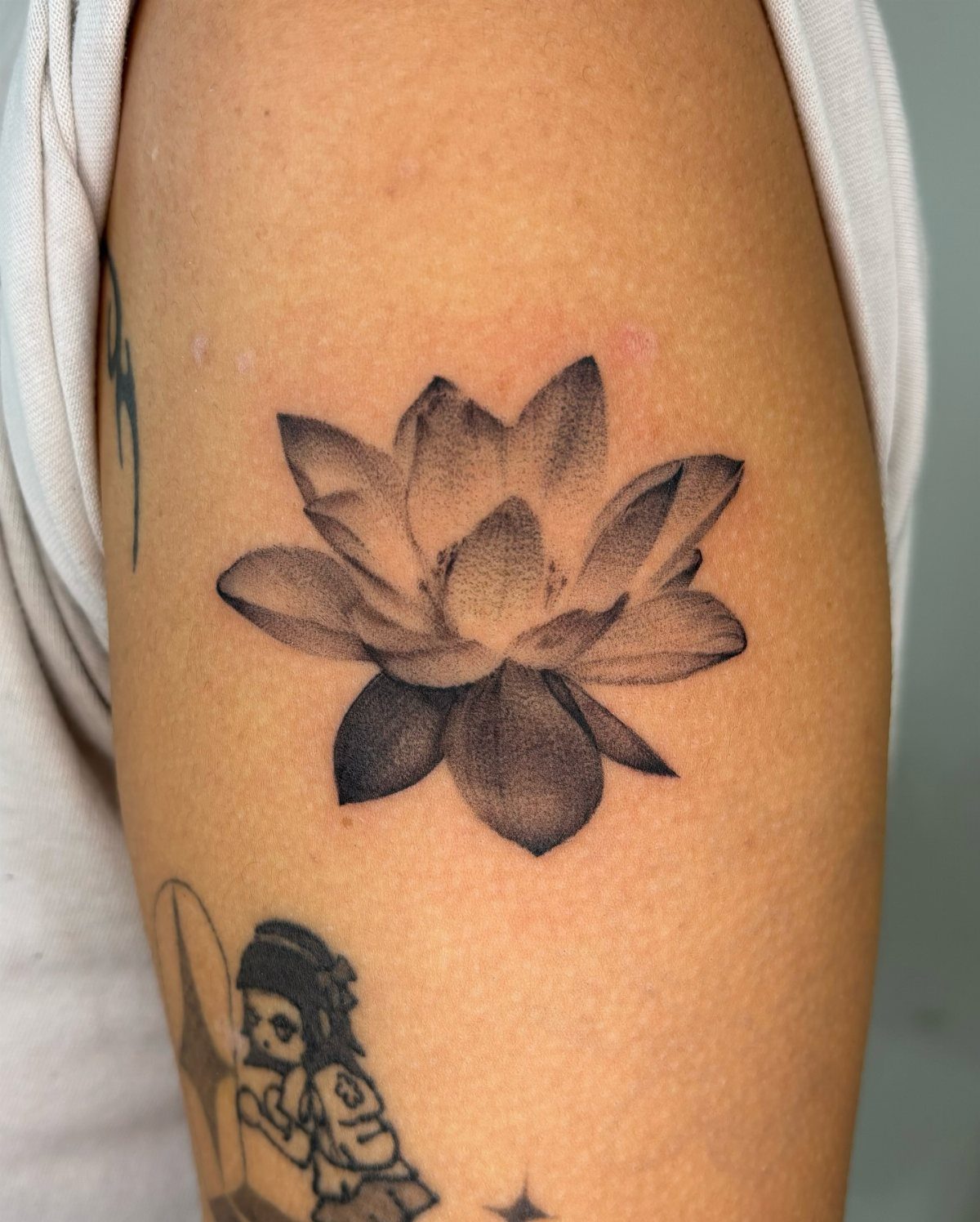 17 Flower Tattoo Ideas That Work in Every Style 1 A realistic black and grey lotus flower tattoo on a person's upper arm skin.