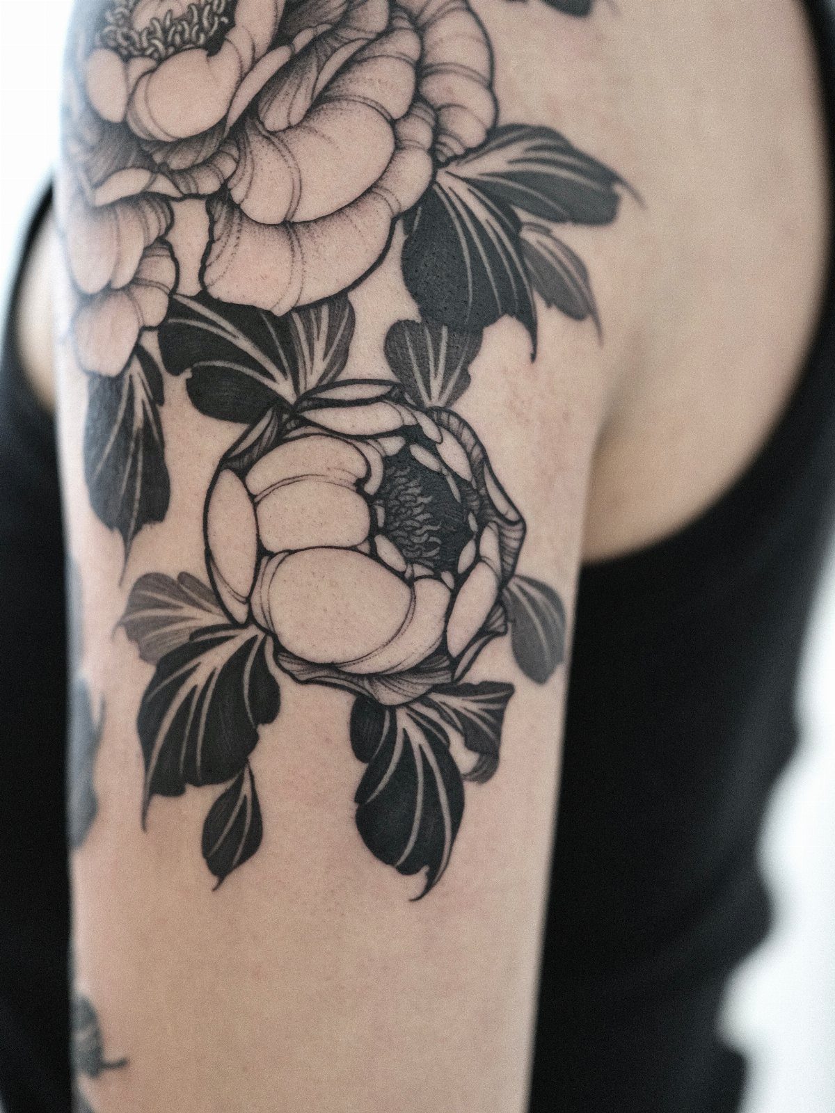 17 Flower Tattoo Ideas That Work in Every Style 5 Large black and grey peony tattoo with detailed petals and leaves on a person's arm.