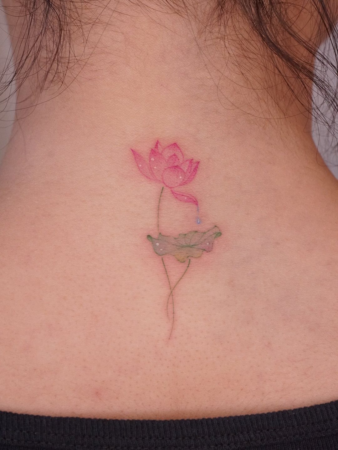 17 Flower Tattoo Ideas That Work in Every Style 13 A pink watercolor lotus flower tattoo with a green leaf on a person's neck.